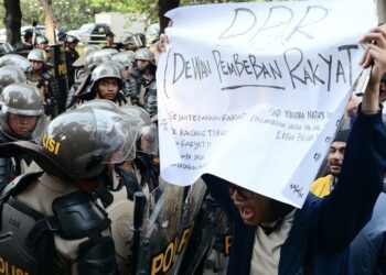 Amnesty International Desak Pemerintah Usut Kematian 10 Warga dan Bebaskan Aktivis HAM Seorang mahasiswa yang membentangkan poster protes terhadap DPR di hadapan polisi dalam aksi unjuk rasa Agustus 2025 di Jakarta. (Foto: Iqro Rinaldi via Unsplash)
